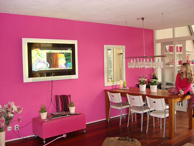 A tastefully decorated pink-painted open space dining area with chandelier and young girl sitting on the table watching a flat screen TV. Photo credit: koekiehaas on Flickr.